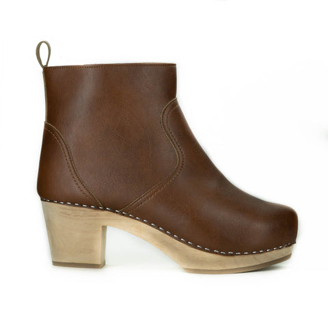 A tan vegan leather clog bootie. Ankle height shaft with pull tab in back. Inside zipper closure. Blonde wooden sole. Staples around outsole to connect material to sole.