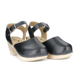 A mary jane style clog in black vegan leather. Ankle strap with silver buckle closure. Cork lining and blonde wood sole and heel. Silver staples attached upper to sole.