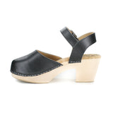 A mary jane style clog in black vegan leather. Ankle strap with silver buckle closure. Cork lining and blonde wood sole and heel. Silver staples attached upper to sole.